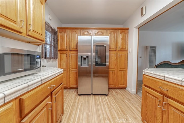 kitchen featuring appliances with stainless steel finishes, tile counters, and light wood-type flooring