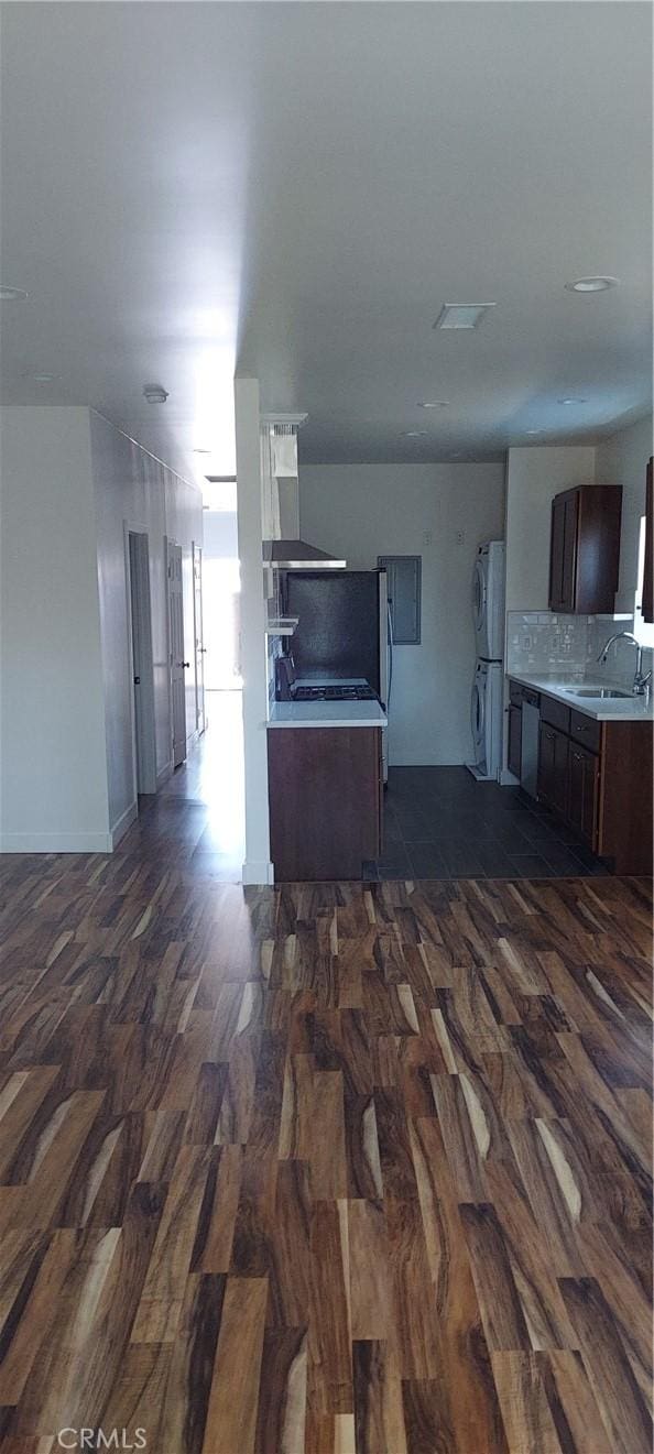 kitchen with stacked washer and clothes dryer, light countertops, dark wood-type flooring, a sink, and wall chimney range hood