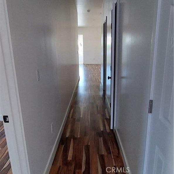 corridor with baseboards and dark wood-style flooring