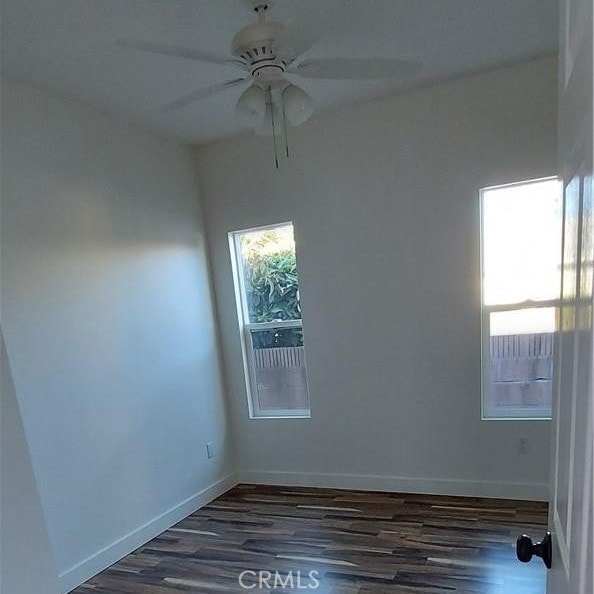 empty room featuring ceiling fan, baseboards, and dark wood-style floors