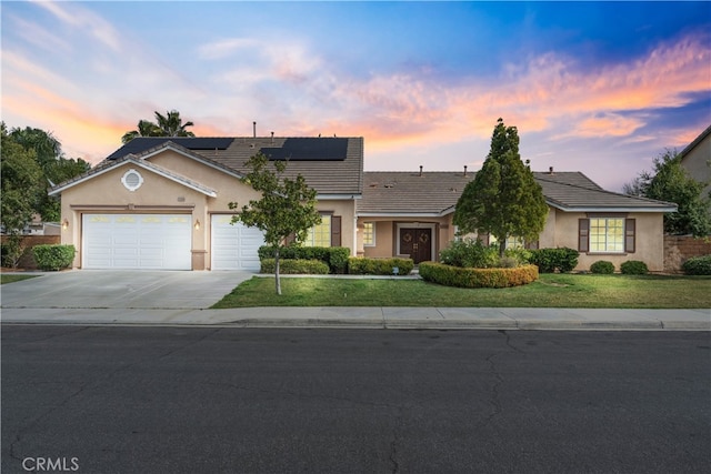 view of front of home featuring a garage, a yard, and solar panels