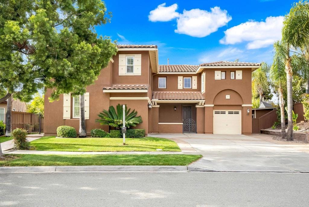 mediterranean / spanish home with fence, driveway, a tiled roof, stucco siding, and a front yard