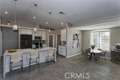 kitchen with black refrigerator, pendant lighting, an island with sink, white cabinets, and a kitchen bar