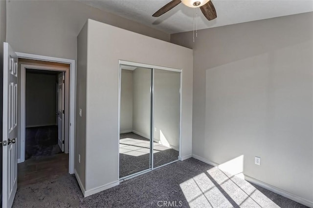 unfurnished bedroom with dark colored carpet, ceiling fan, and a closet