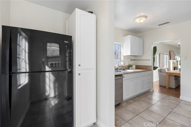 kitchen featuring visible vents, stainless steel dishwasher, freestanding refrigerator, white cabinets, and a sink