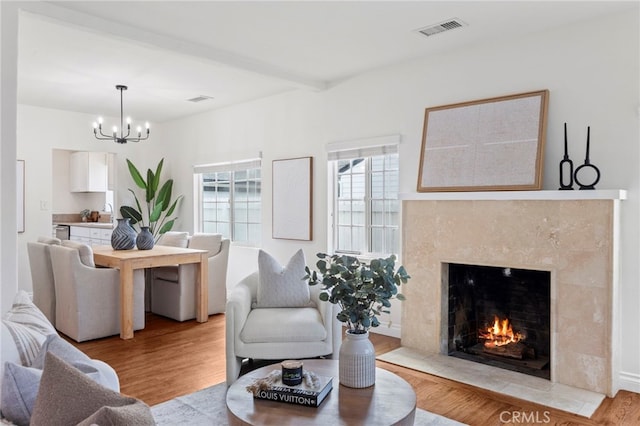 living area featuring visible vents, an inviting chandelier, a high end fireplace, light wood-style floors, and beamed ceiling