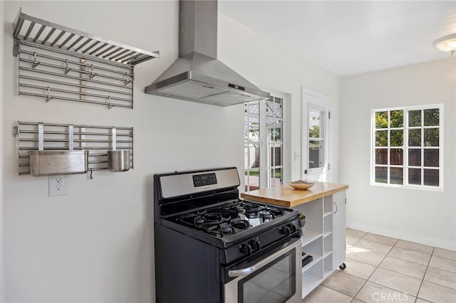 kitchen with baseboards, stainless steel range with gas stovetop, range hood, light tile patterned flooring, and open shelves