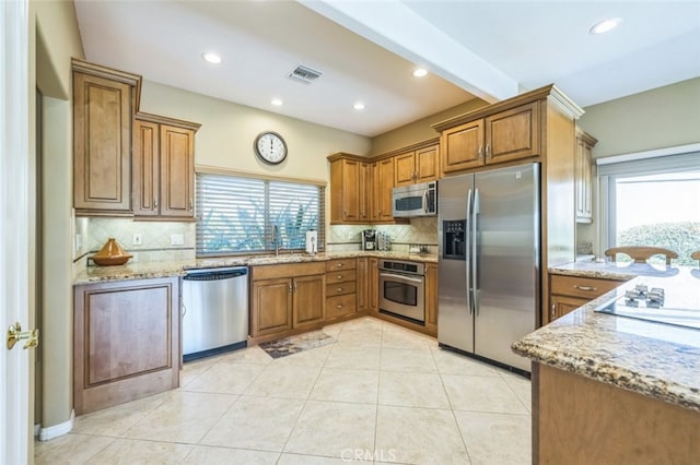 kitchen with light stone counters, appliances with stainless steel finishes, sink, and beamed ceiling