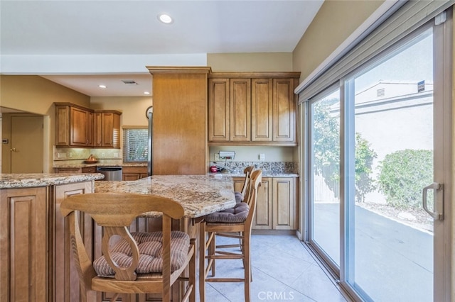 kitchen with tasteful backsplash, dishwasher, a kitchen bar, light tile patterned floors, and light stone countertops