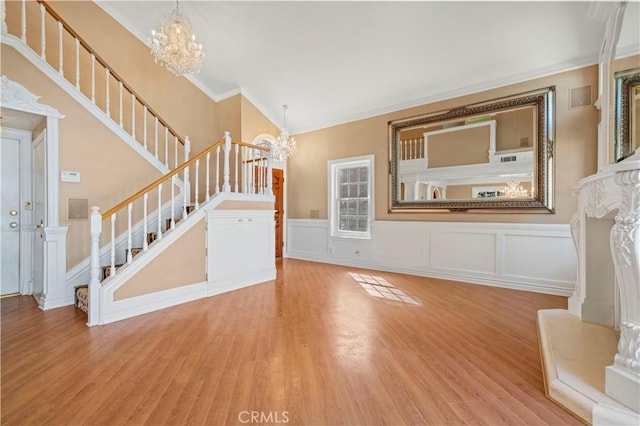 unfurnished living room with ornamental molding, a chandelier, stairs, and light wood finished floors