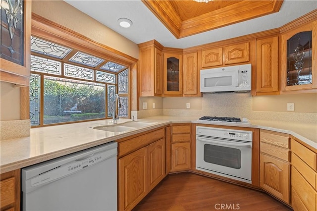 kitchen featuring white appliances, dark wood finished floors, a sink, light countertops, and a raised ceiling