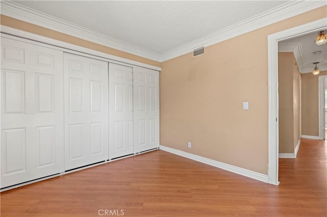 unfurnished bedroom featuring baseboards, attic access, ornamental molding, light wood-style flooring, and a closet