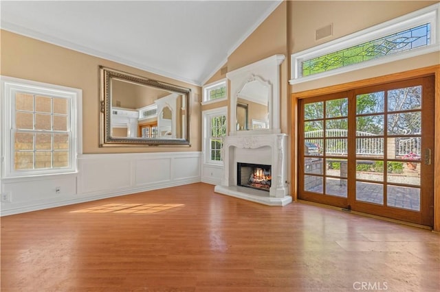 unfurnished living room featuring plenty of natural light, a warm lit fireplace, wood finished floors, and vaulted ceiling