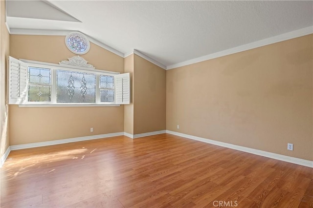 unfurnished room featuring wood finished floors, baseboards, lofted ceiling, a textured ceiling, and crown molding