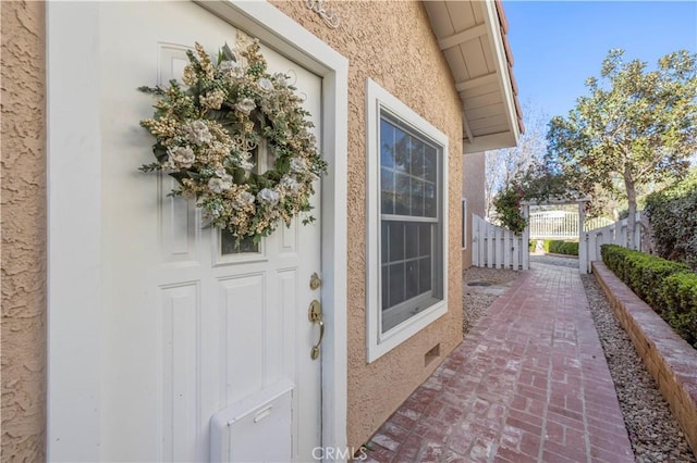 view of exterior entry featuring fence and stucco siding