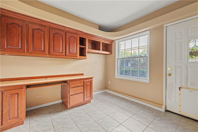 unfurnished office featuring light tile patterned floors, built in desk, and baseboards