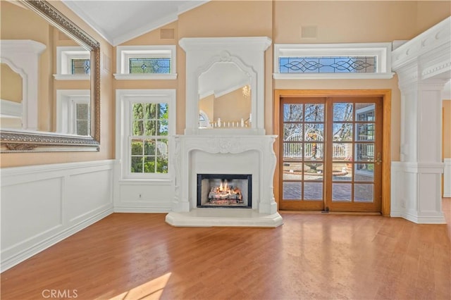 unfurnished living room with wood finished floors, decorative columns, a warm lit fireplace, vaulted ceiling, and a decorative wall