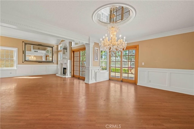 interior space with wood finished floors, decorative columns, a fireplace with raised hearth, and a chandelier