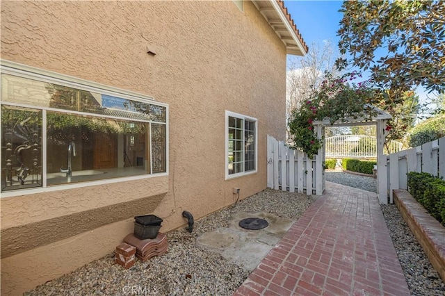 view of side of property featuring a gate, fence, and stucco siding