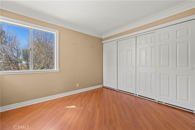 unfurnished bedroom featuring a closet, light wood-type flooring, baseboards, and ornamental molding