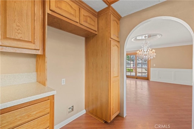 kitchen with an inviting chandelier, arched walkways, light countertops, light wood-style floors, and wainscoting