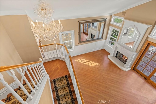 staircase featuring a glass covered fireplace, wood finished floors, a chandelier, and ornamental molding