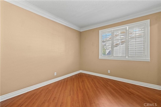 empty room featuring crown molding, baseboards, and wood finished floors