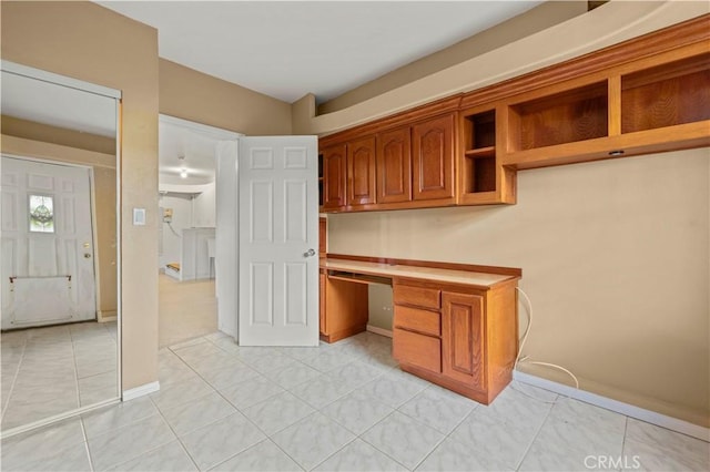 unfurnished office featuring light tile patterned floors, built in desk, and baseboards