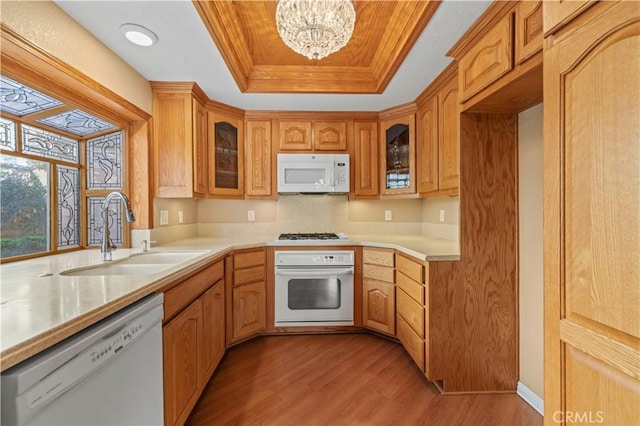 kitchen featuring light wood finished floors, light countertops, white appliances, a raised ceiling, and a sink