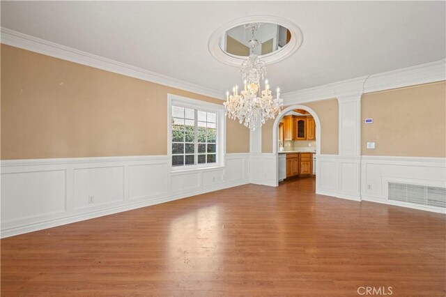 empty room with visible vents, crown molding, a chandelier, wood finished floors, and arched walkways