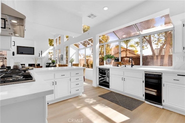 kitchen featuring black gas cooktop, light countertops, a sink, light wood-type flooring, and beverage cooler