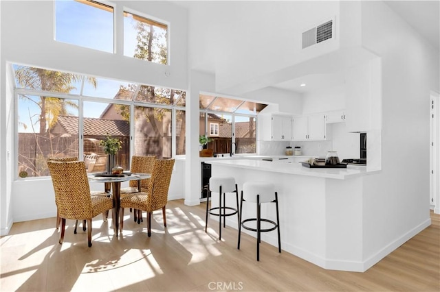 kitchen featuring visible vents, white cabinets, a high ceiling, light countertops, and light wood-style floors