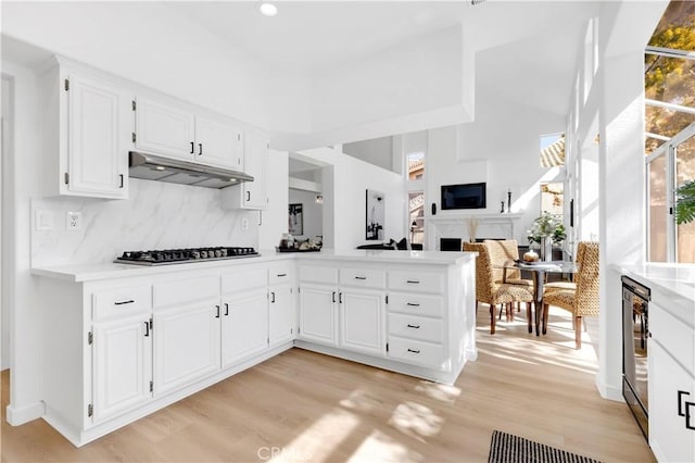 kitchen with light wood-style floors, light countertops, under cabinet range hood, stainless steel gas cooktop, and backsplash