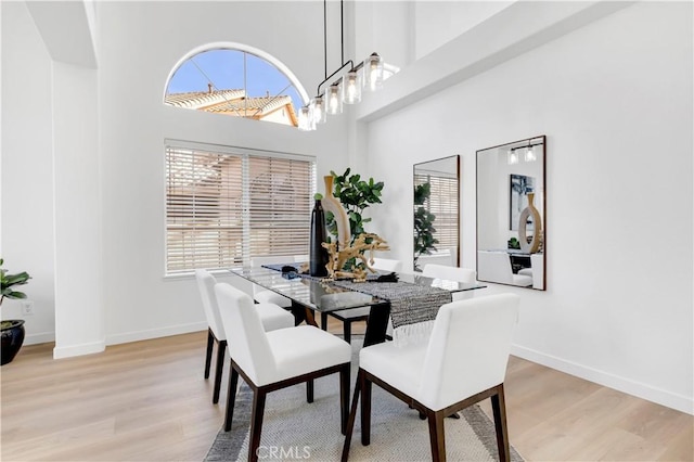 dining room featuring a towering ceiling, light wood-style flooring, and baseboards