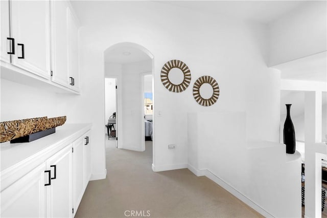 hallway featuring light carpet, baseboards, and arched walkways