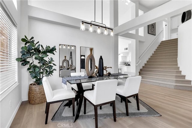 dining space featuring stairs, a high ceiling, wood finished floors, and baseboards