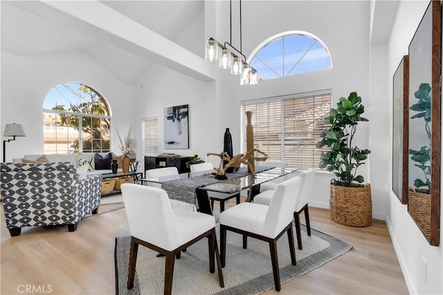 dining area featuring a chandelier, high vaulted ceiling, baseboards, and light wood-style floors