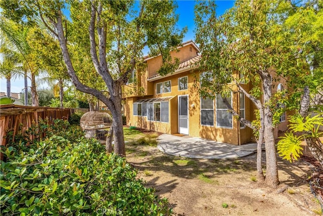 rear view of house featuring a patio area, fence, and stucco siding