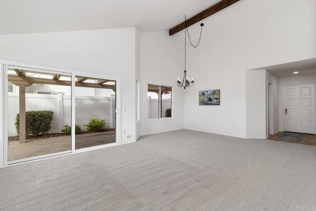 unfurnished living room with beamed ceiling, high vaulted ceiling, carpet floors, and a notable chandelier