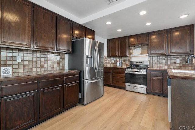 kitchen featuring sink, appliances with stainless steel finishes, dark brown cabinets, tile counters, and light hardwood / wood-style floors