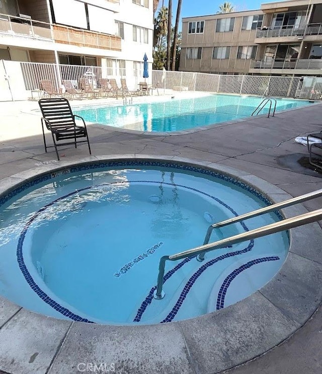 view of swimming pool with a community hot tub and fence