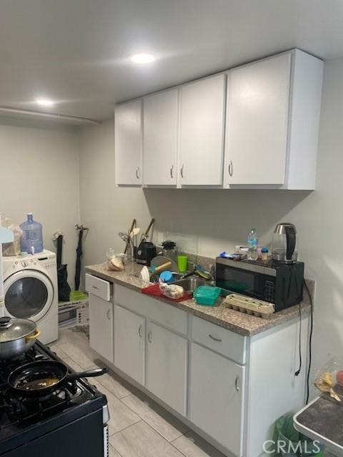 kitchen featuring light tile patterned floors, white cabinetry, range with gas stovetop, light stone countertops, and washer / dryer