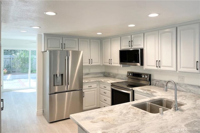 kitchen with appliances with stainless steel finishes, a sink, white cabinets, and light stone countertops