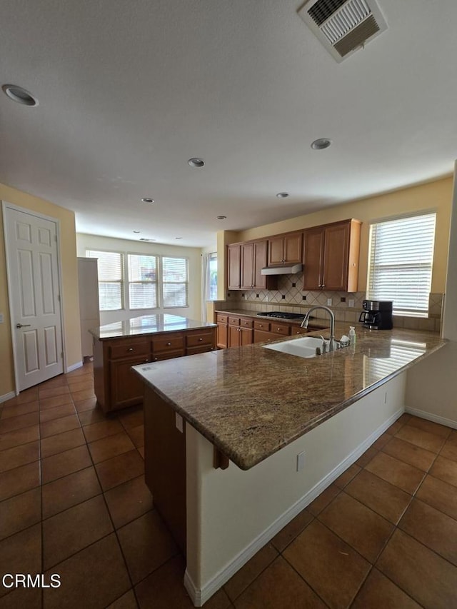 kitchen featuring a breakfast bar, sink, stainless steel gas cooktop, kitchen peninsula, and decorative backsplash