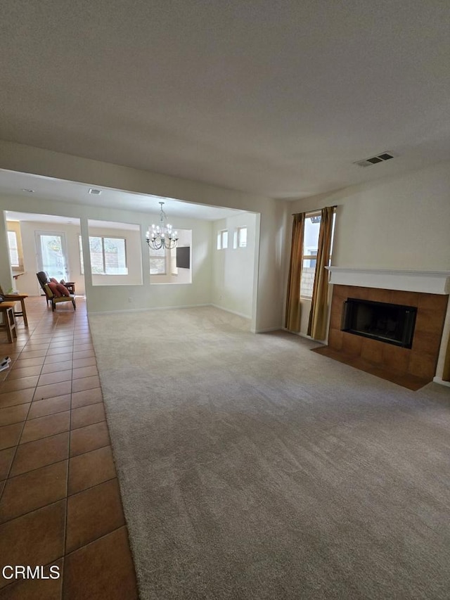 unfurnished living room featuring carpet flooring, a chandelier, and a tile fireplace