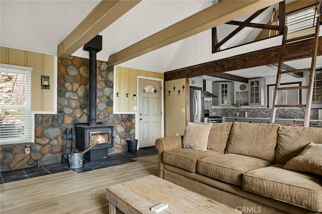 living area with beam ceiling, high vaulted ceiling, wood finished floors, and a wood stove