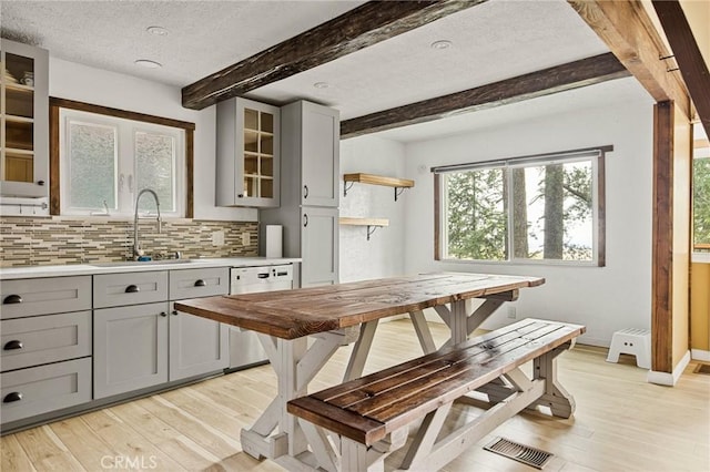 kitchen with a sink, gray cabinetry, light wood-style floors, dishwasher, and beamed ceiling