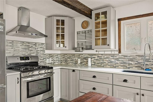 kitchen with beamed ceiling, sink, backsplash, stainless steel gas range oven, and wall chimney exhaust hood