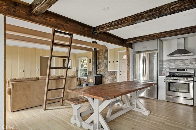 dining area with beamed ceiling, light hardwood / wood-style floors, and a wood stove