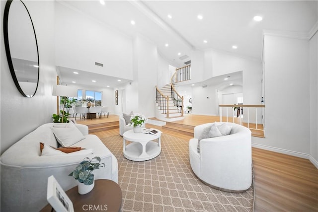 living room with high vaulted ceiling, stairs, visible vents, and wood finished floors